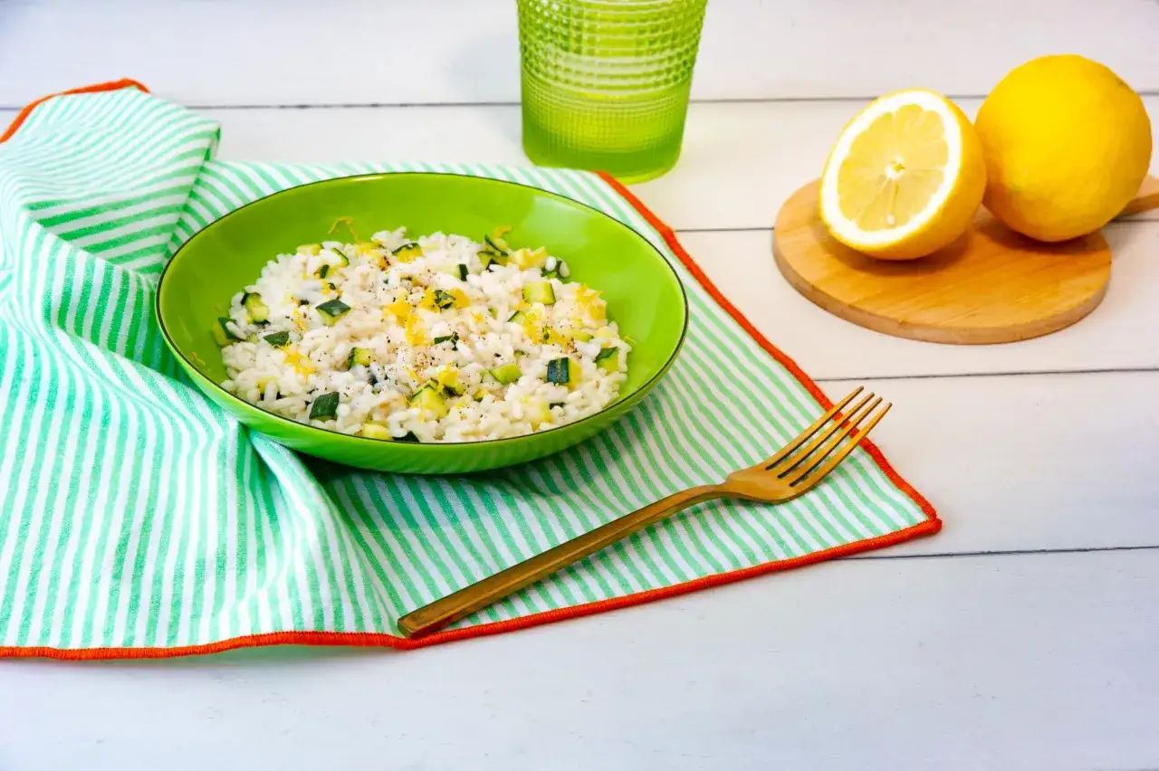 Un piatto di **riso zucchine e limone** profumato, guarnito con scorza di limone e pepe nero, pronto per essere gustato.