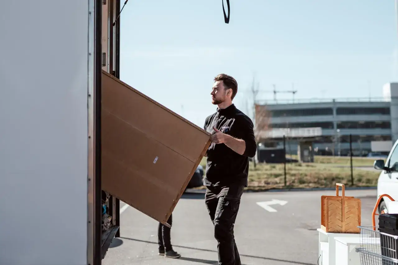 Man hjälper till att packa tavlor för flytt. En stor kartong bärs in i en flyttbil.