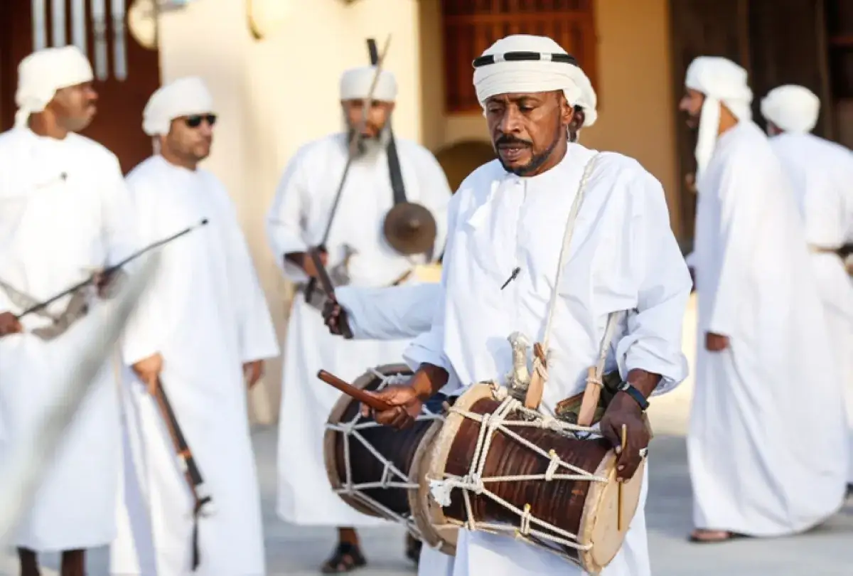 Männer in traditioneller Kleidung spielen Trommeln und halten Gewehre, ein lebendiges Bild der omanischen Kultur.