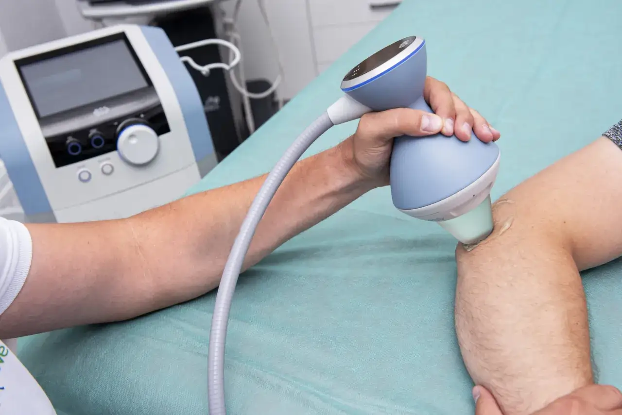 Terapia falą uderzeniową na łokieć tenisisty. Fizjoterapeuta aplikuje żel i głowicę aparatu na bolące miejsce.