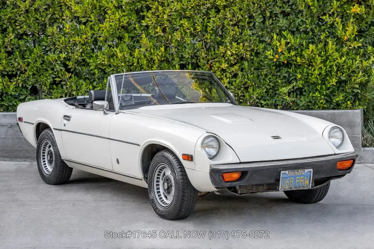 Vit cabriolet Jensen Healey parkerad framf&ouml;r en gr&ouml;n h&auml;ck.