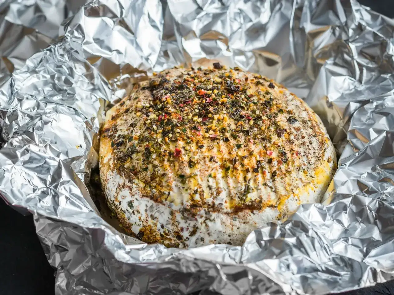 Pyszny camembert z grilla, otulony folią aluminiową, posypany ziołami i przyprawami.