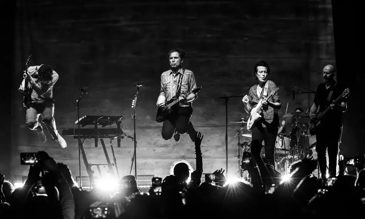 Les membres de Franz Ferdinand en plein concert, un guitariste saute, la foule filme.