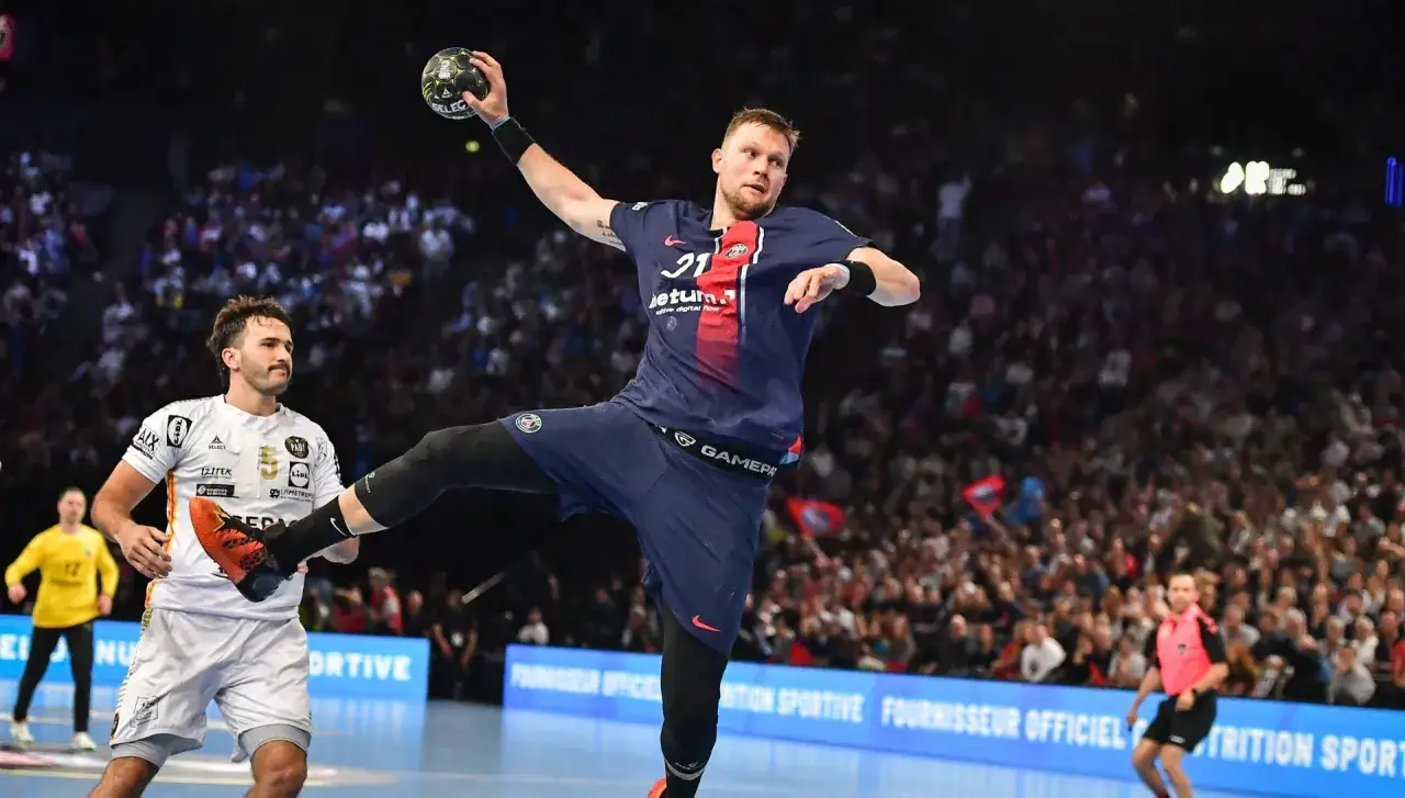 Gracz PSG w skoku do rzutu podczas meczu piłki ręcznej. W tle trybuny pełne kibic&oacute;w.