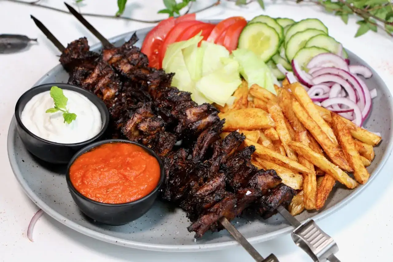 En tallrik med vegetarisk kebab på spett, serverad med pommes frites, sallad, tomat, gurka, rödlök och två dippsåser.