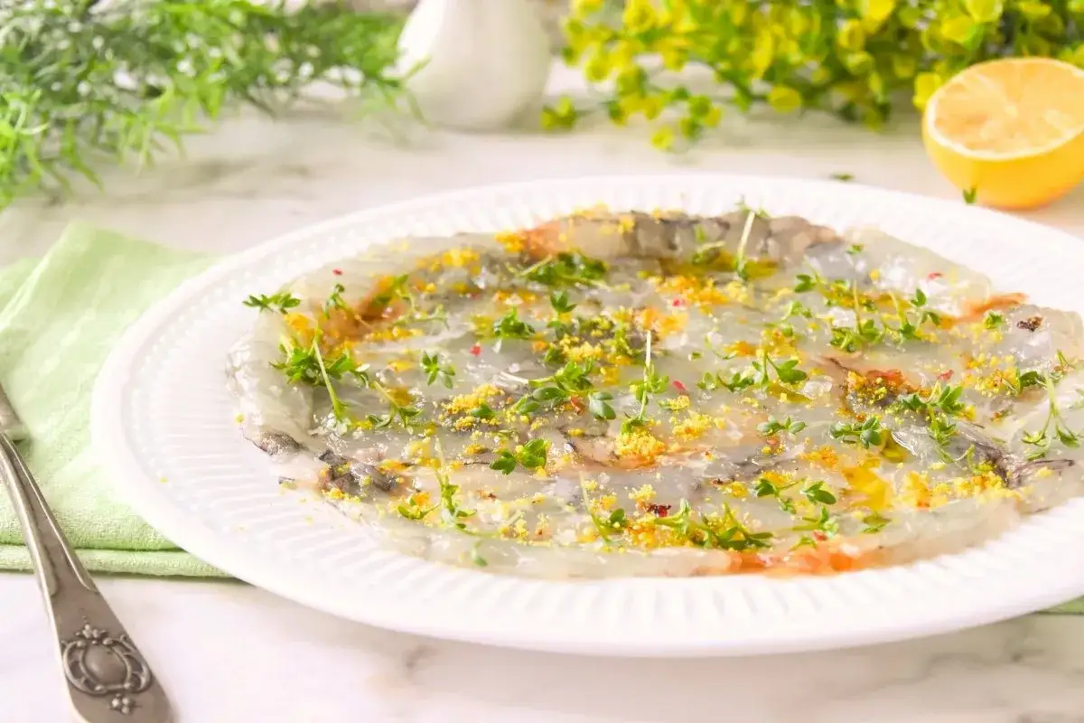 Delicado carpaccio de gambas con hierbas frescas y ralladura de lim&oacute;n, listo para disfrutar.