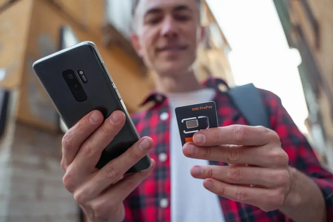 Młody mężczyzna trzyma smartfon i kartę SIM. To idealne rozwiązanie dla osób szukających internetu na kartę bez umowy.