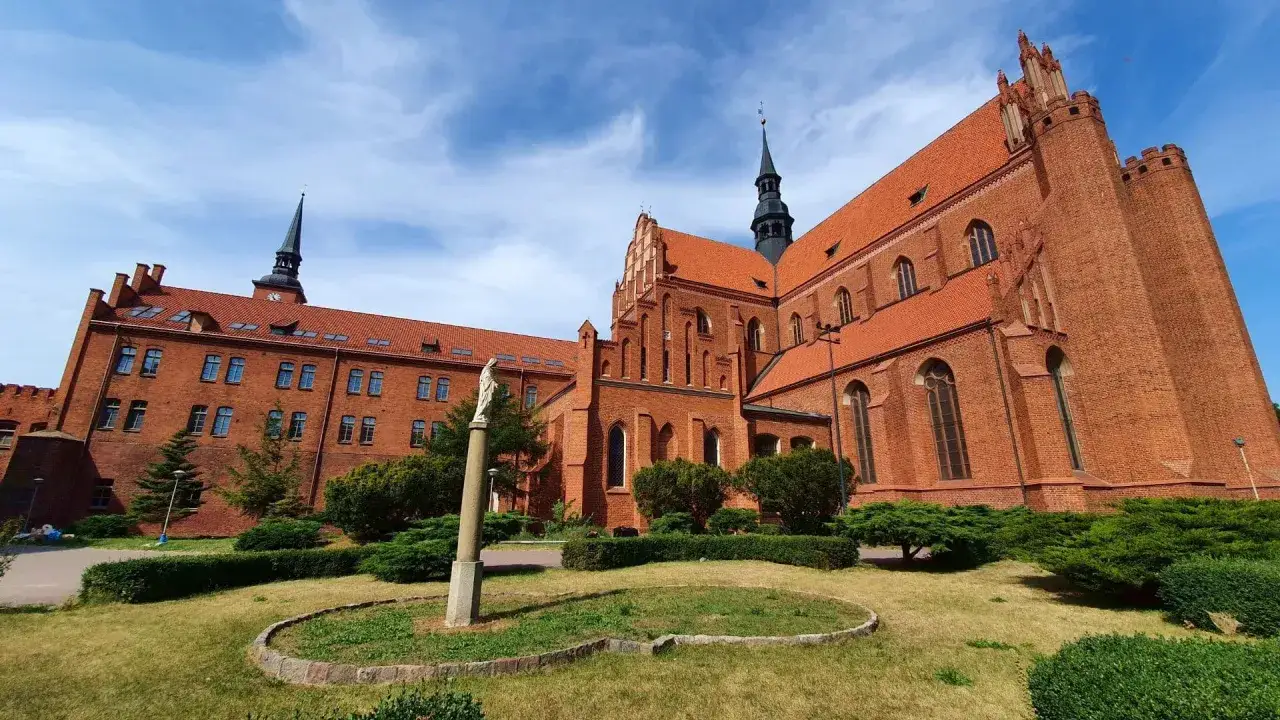 Gotycka ceglana katedra w Pelplinie, serce Kociewia, z zielonym ogrodem i figurą Matki Boskiej.