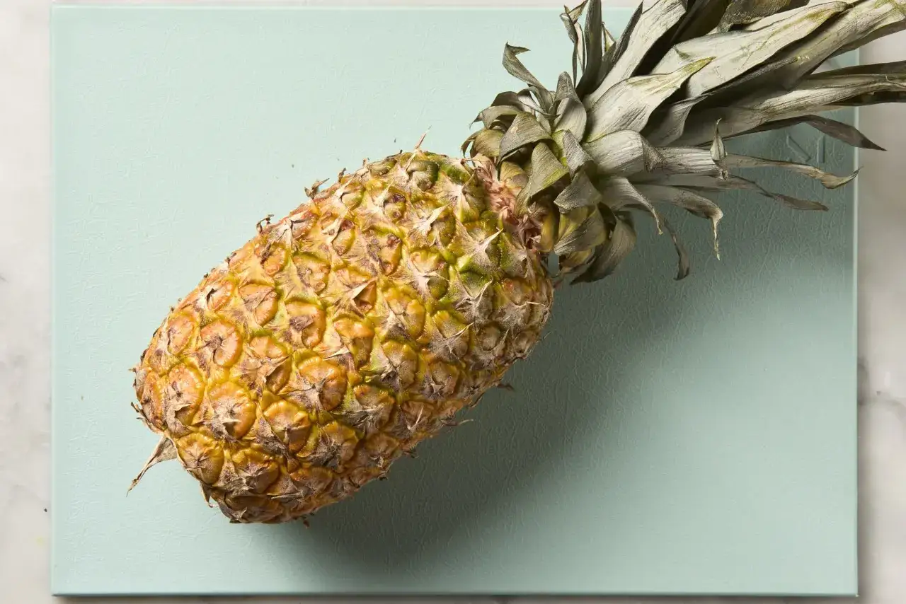 Eine reife Ananas liegt auf einem mintgr&uuml;nen Brett. Sie sieht so saftig aus, man k&ouml;nnte fast meinen, die Ananas schmeckt nach Alkohol.