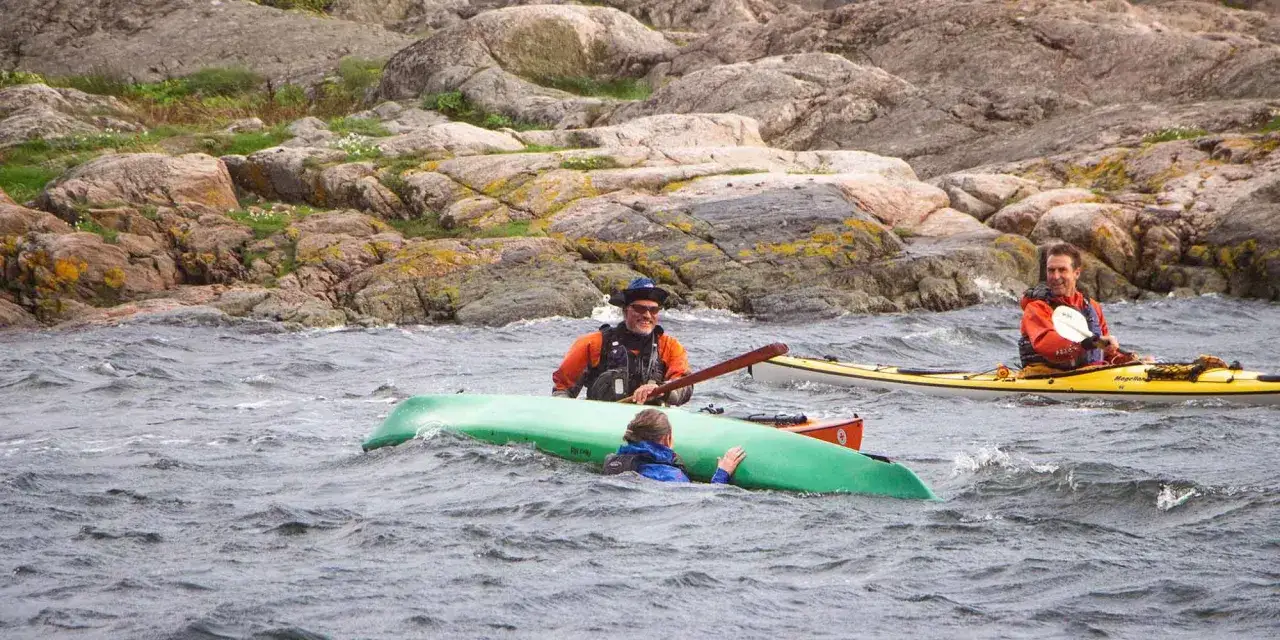 Två män paddlar kajak i skärgården. En person har ramlat ur sin kajak och får hjälp. Bra paddla kajak teknik är viktigt.