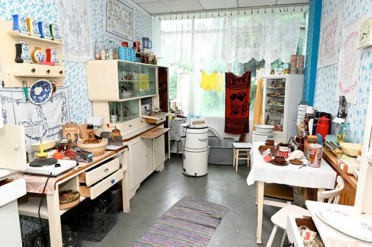 Wnętrze kuchni jak z muzeum sentymentów. Stare meble, pralka, naczynia i tekstylia tworzą nostalgiczną atmosferę.