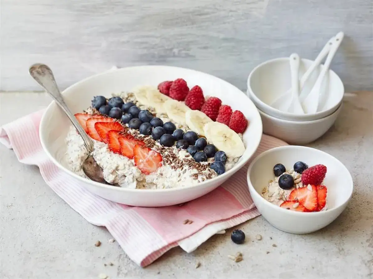 En skål med gröt toppad med jordgubbar, blåbär, hallon och banan. En mindre skål med samma topping. Filmjölk vs kefir – en hälsosam frukost.
