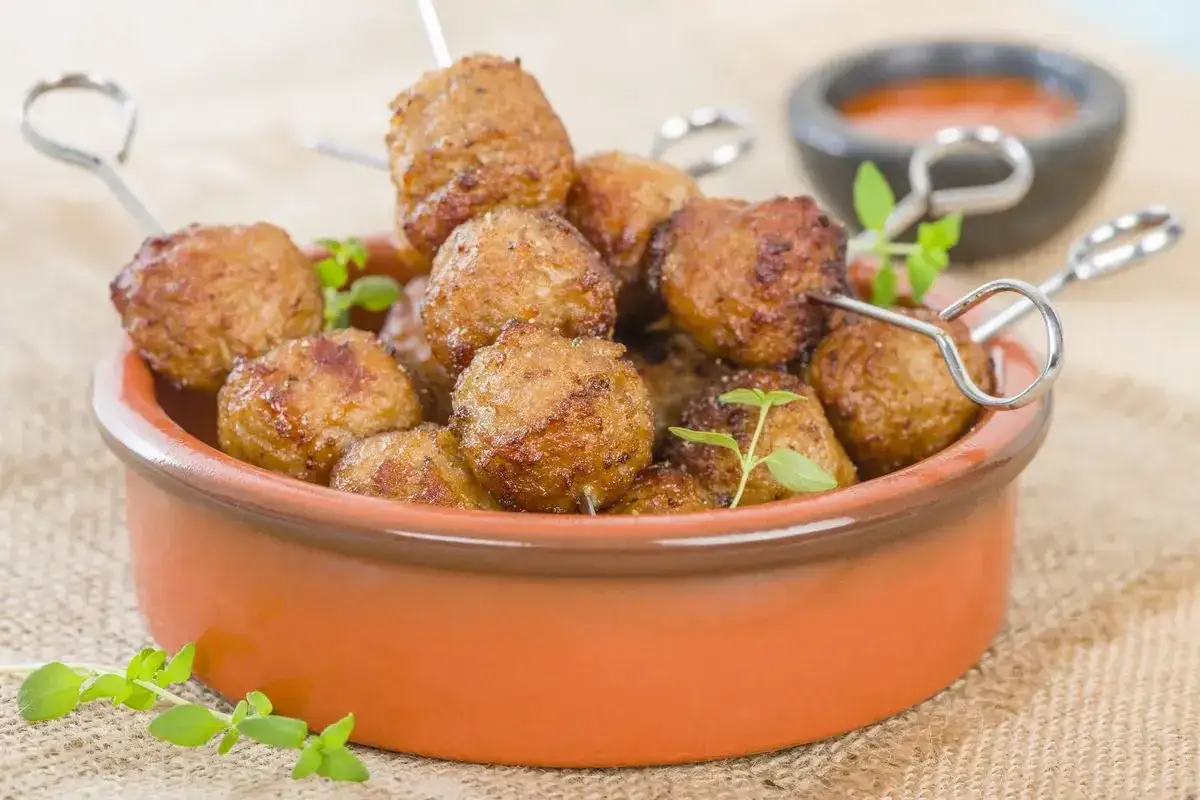 Polpette di tacchino in friggitrice ad aria, dorate e succulente, servite in una ciotola di terracotta con erbe aromatiche.