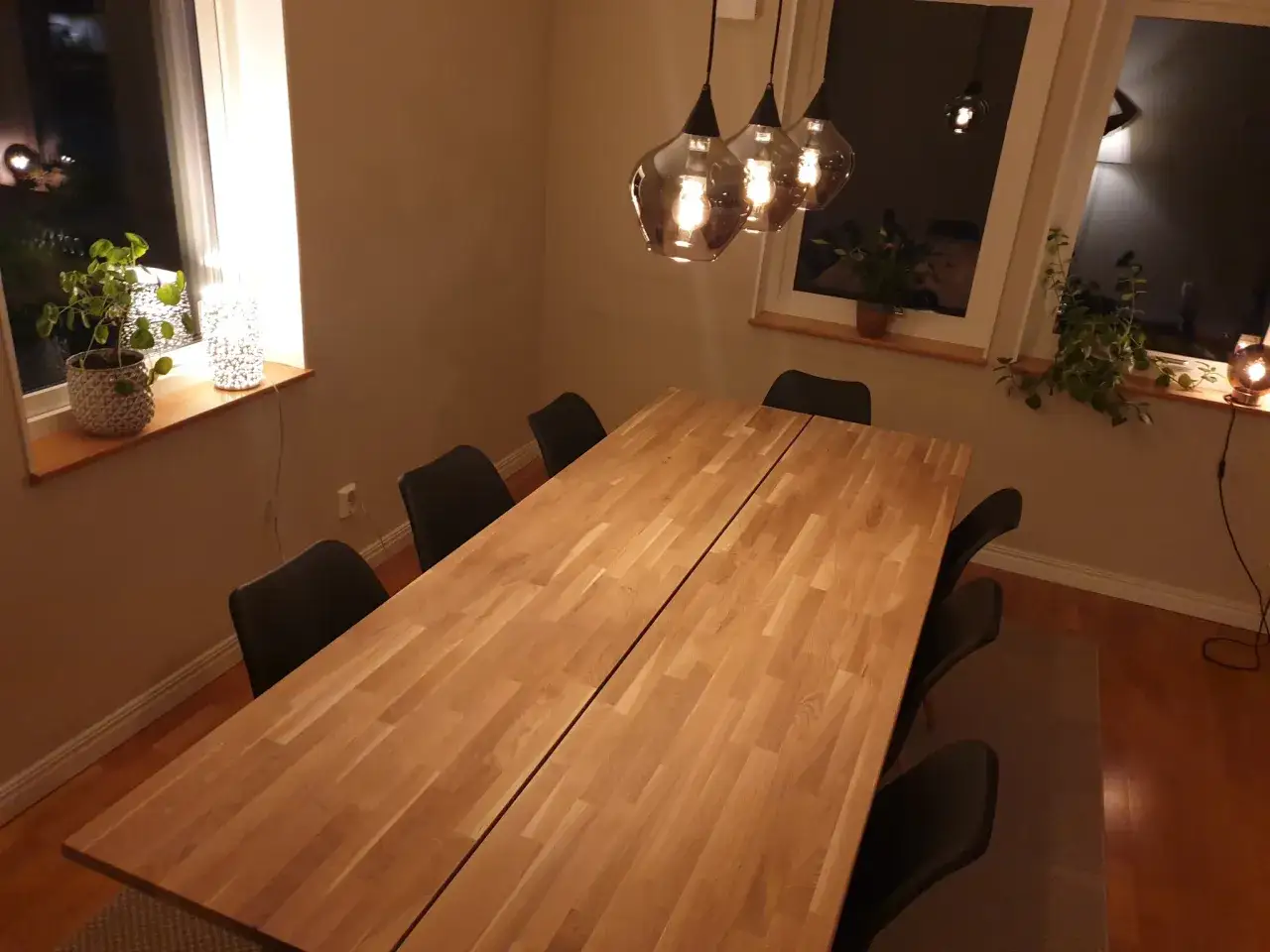 Ett stort matbord i trä, perfekt för att bygga minnen kring. Mörka stolar och mysig belysning skapar en inbjudande atmosfär.