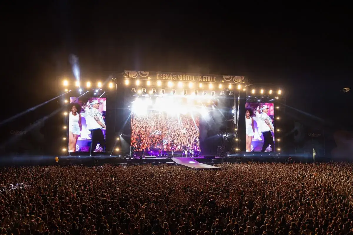 Macklemore na scenie w Polsce, tłum szaleje pod sceną, światła i ekrany tworzą niesamowity klimat koncertu.
