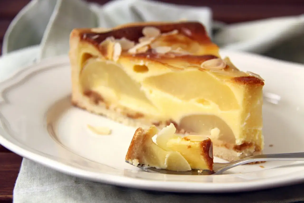 Une part de tarte aux poires au sirop, garnie d'amandes effil&eacute;es, sur une assiette blanche.