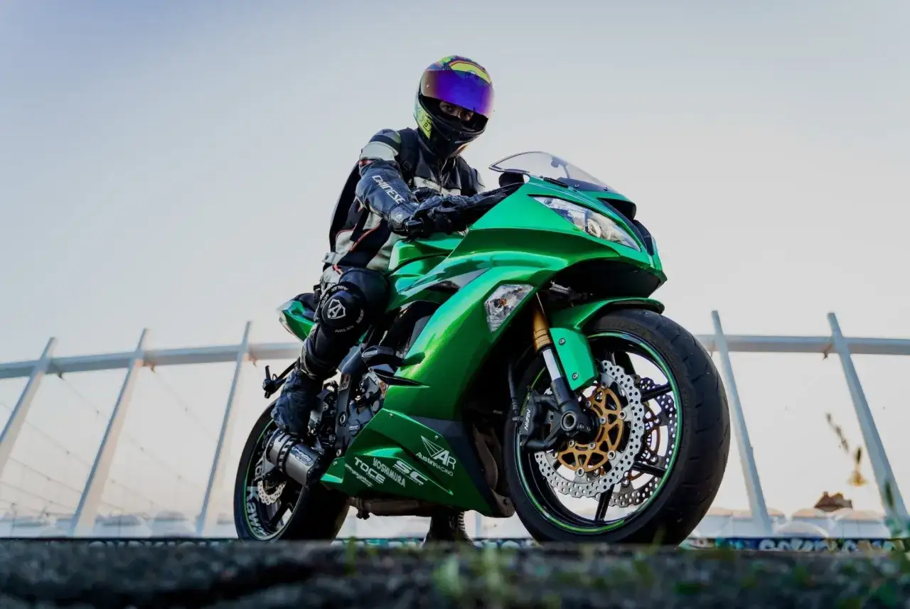 Motociclista con equipo de protección y casco, montando una moto verde brillante con un llamativo carenado de protección.