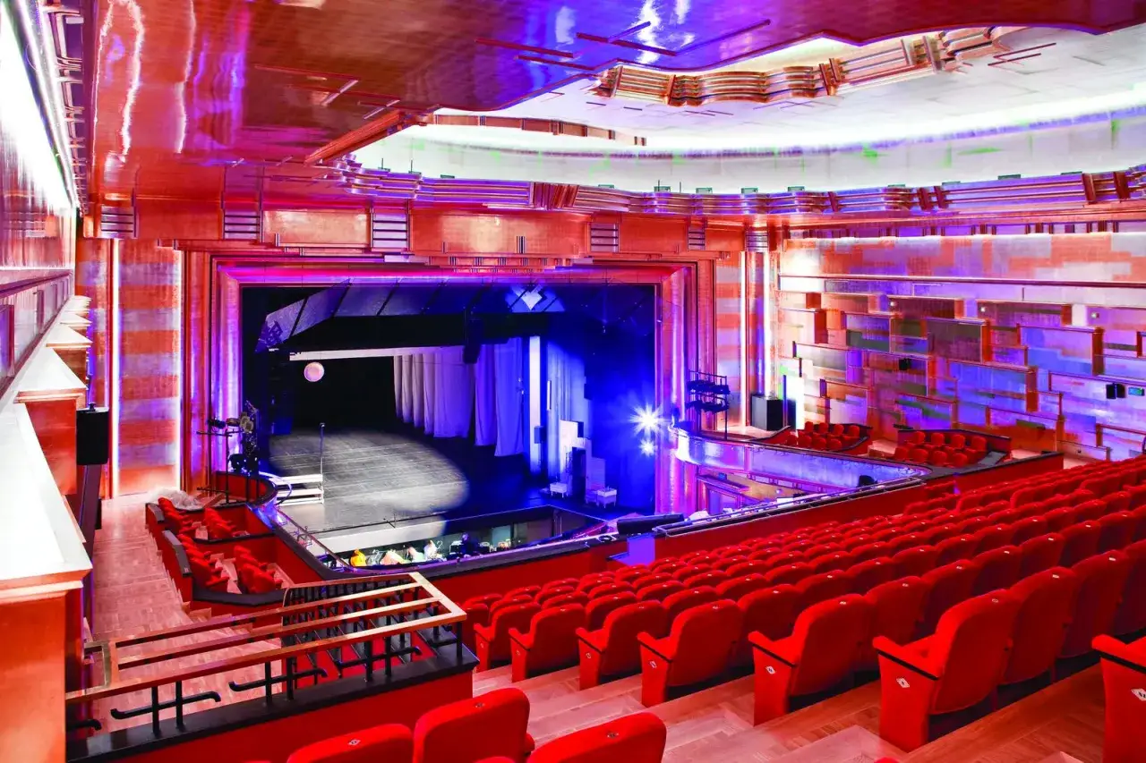 Widownia Teatru Capitol w całej okazałości. Czerwone fotele czekają na widzów, a scena oświetlona jest niebieskim blaskiem.