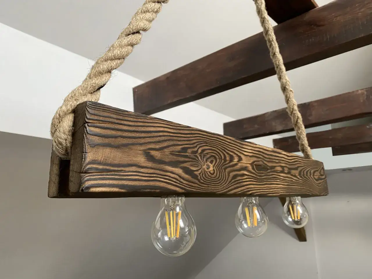 Drewniana belka w stylu loft, zawieszona na grubym sznurze, z trzema żarówkami Edisona.