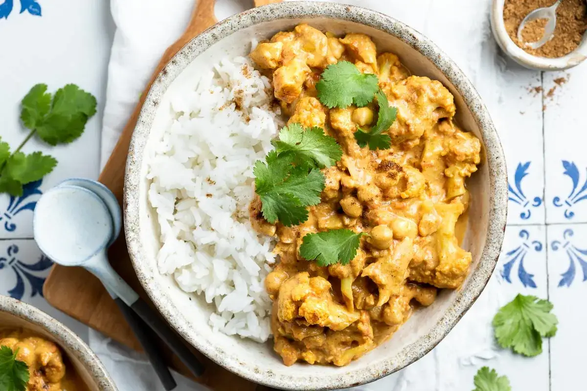 Aksamitne curry z kalafiora i ciecierzycy, podane z ryżem i świeżą kolendrą. Idealne danie dla miłośników aromatycznych smaków.