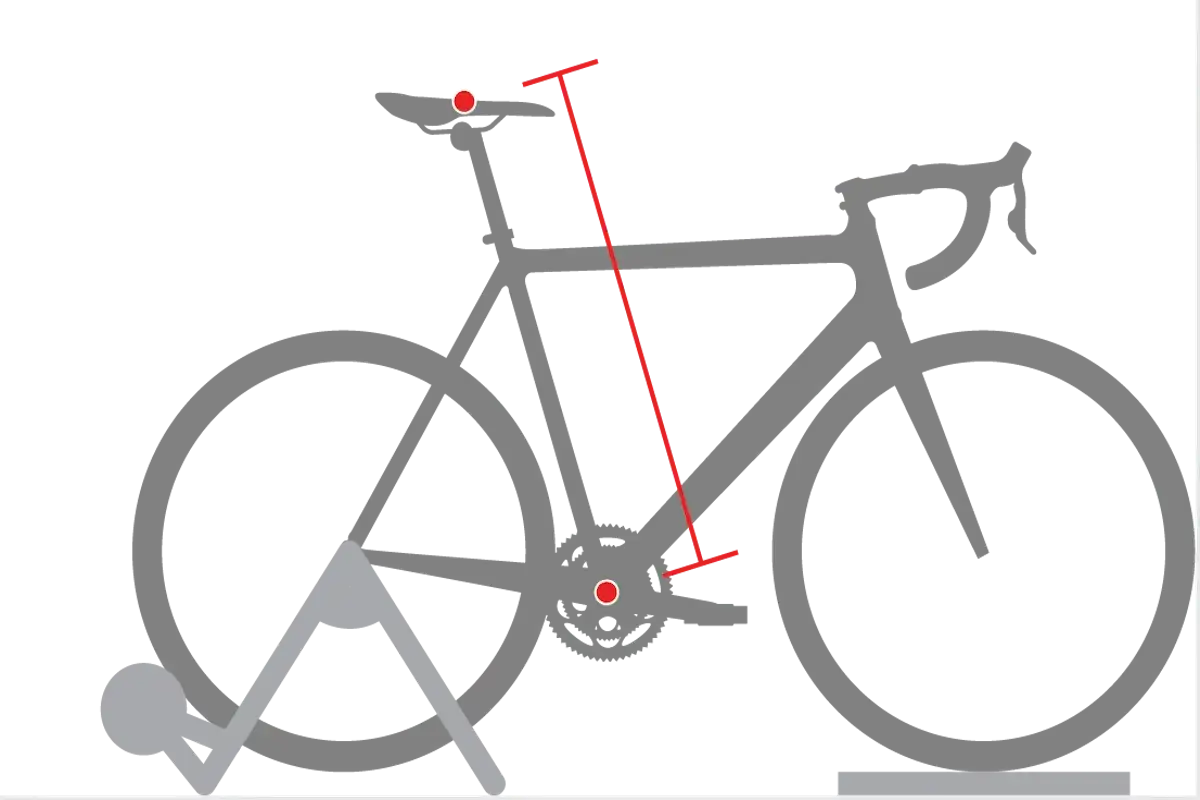 Diagram illustrating proper bike seat height measurement. A red line shows the distance from the pedal spindle to the top of the saddle.