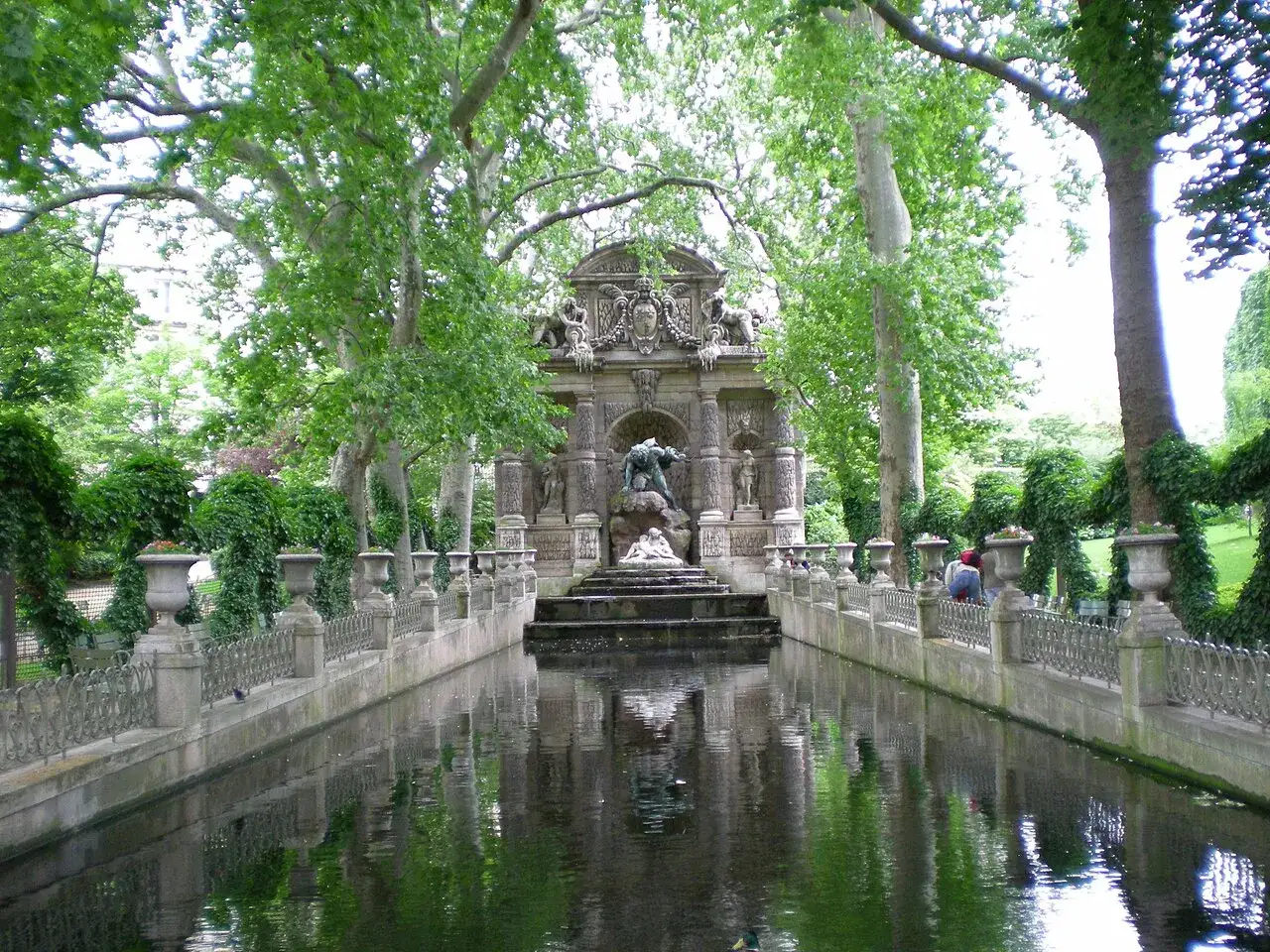 Estanque sereno en los jardines de Luxemburgo, con una fuente monumental y &aacute;rboles frondosos.