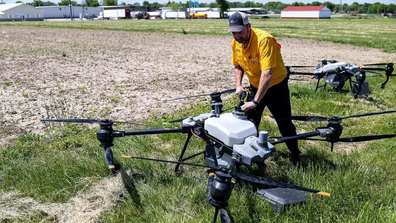 A farmer prepares a drone, one of the types of drones in agriculture, for spraying crops in a field.