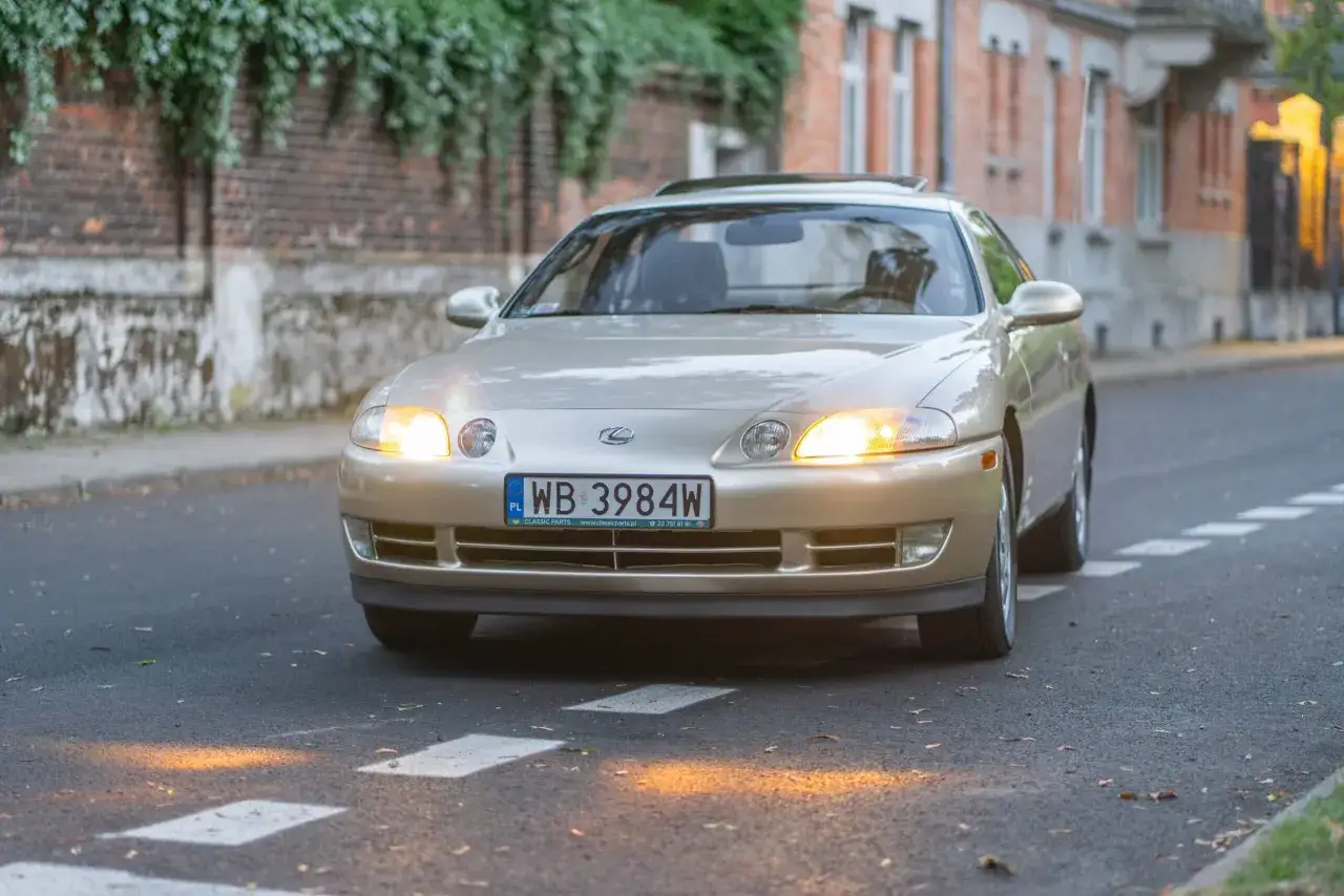 Złoty Lexus SC400 z włączonymi światłami mijania jedzie ulicą.