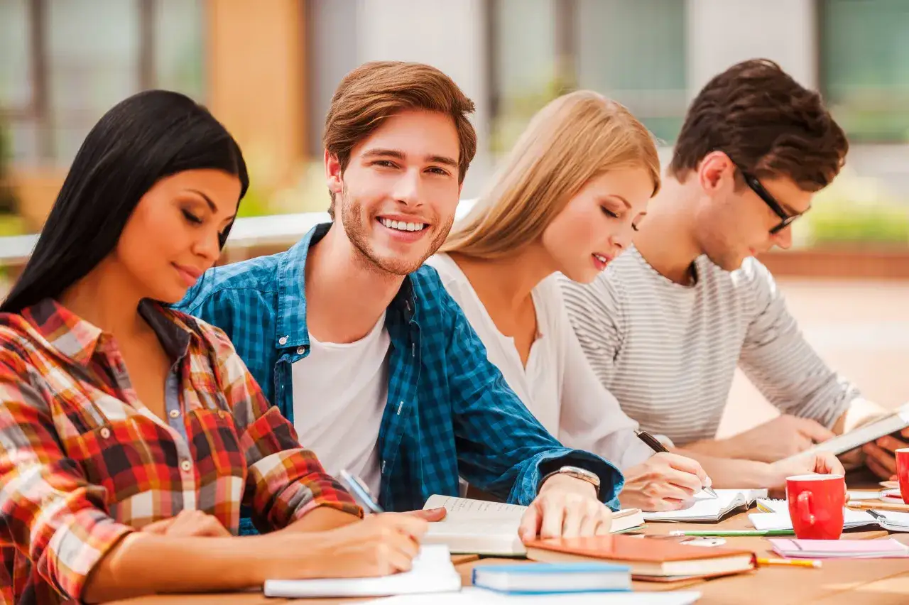 Uśmiechnięty student i jego koledzy uczą się na zewnątrz. Zastanawiasz się, ile trwa technikum po zawodówce?