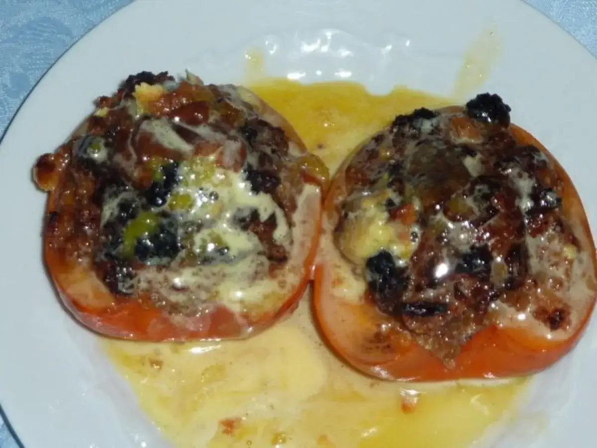 Zwei gefüllte Tomaten, die an eine süße persimmon fruit erinnern, schwimmen in einer goldenen Sauce.