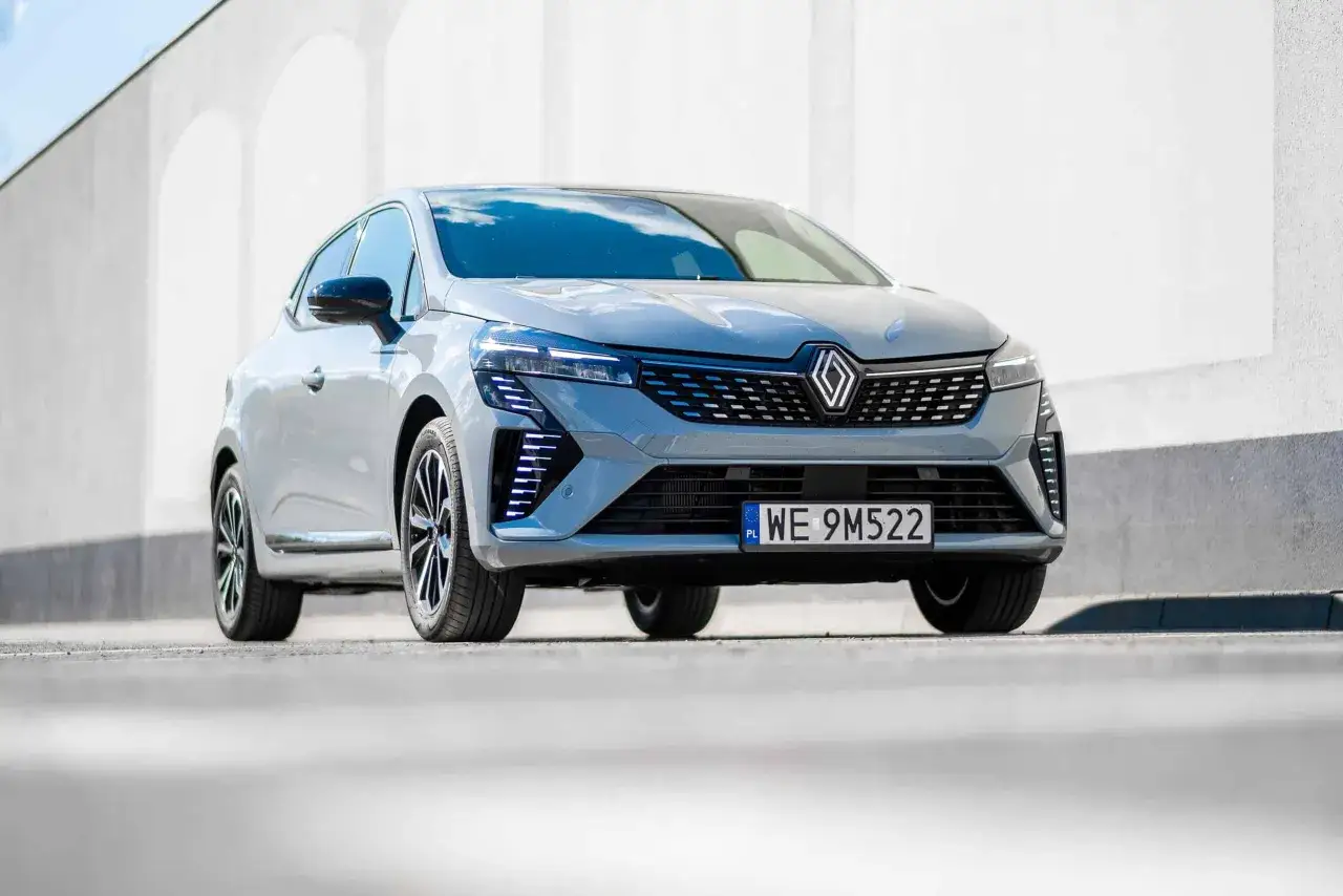 Nowoczesny Renault Clio 2024 w szarym kolorze prezentuje się dynamicznie na tle białej ściany.