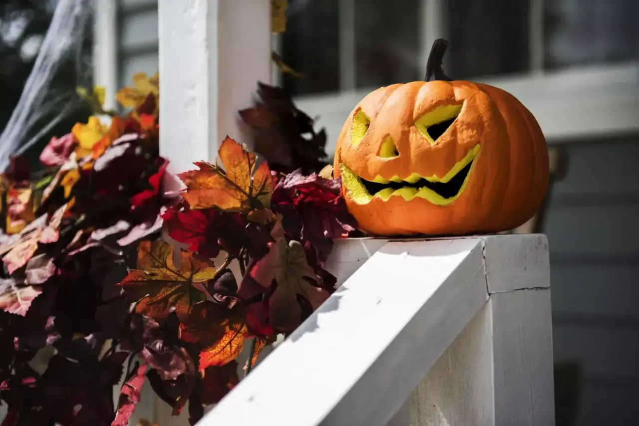 Uśmiechnięta dynia na Halloween, otoczona jesiennymi liśćmi. To pokazuje, co można zrobić z dyni, tworząc dekoracje.