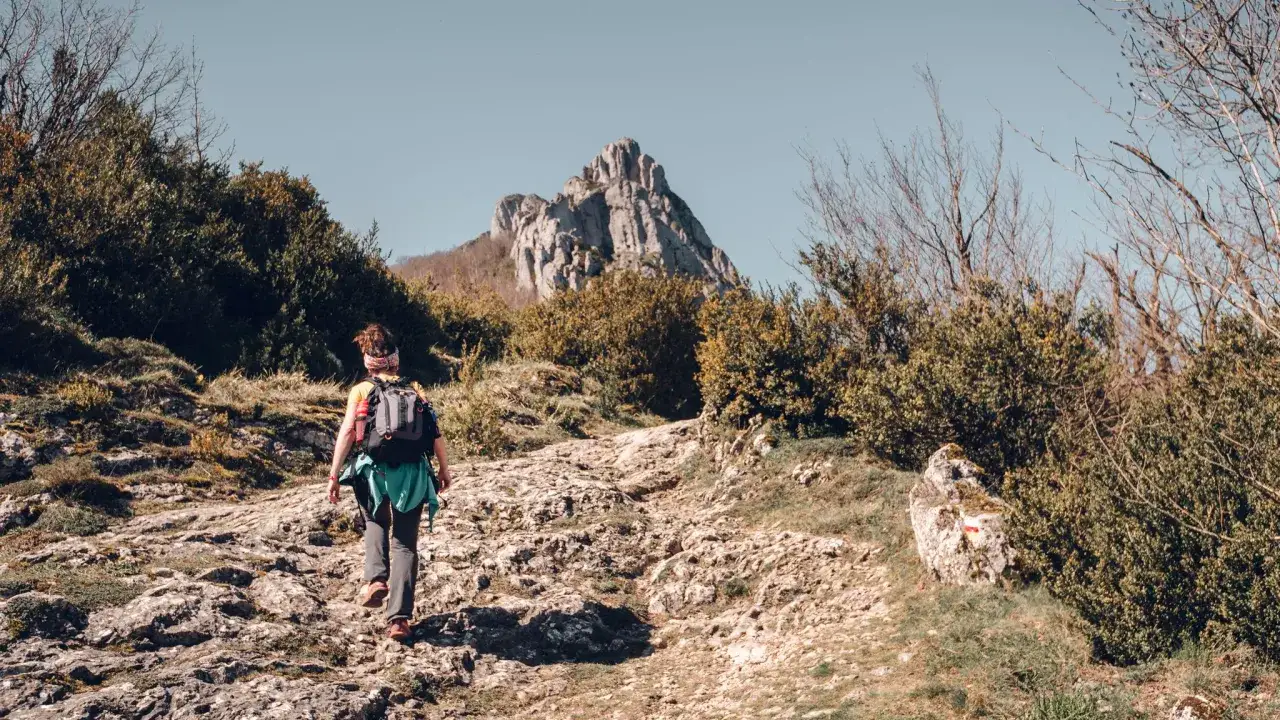 Senderista asciende por un camino rocoso hacia un pico monta&ntilde;oso, disfrutando de las rutas por Burgos.