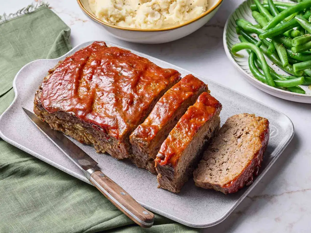 Un plat de pain de viande appétissant, glacé d'une sauce tomate, servi avec des haricots verts et de la purée de pommes de terre. Un repas réconfortant prêt à être dégusté.