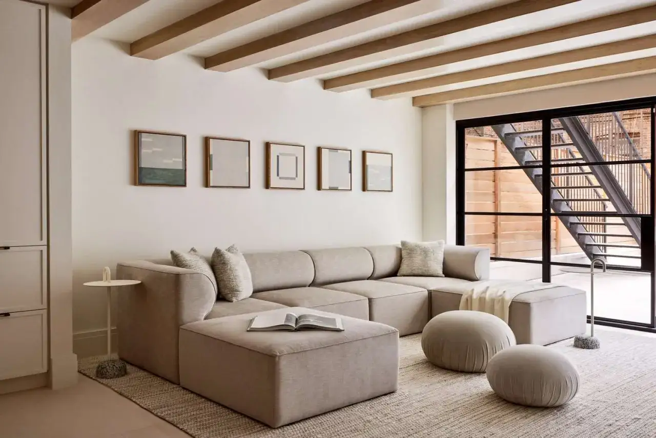 Salon moderne aux teintes &eacute;cru et blanc cass&eacute;. Canap&eacute; modulable, poufs ronds et &oelig;uvres d'art abstraites sur le mur.