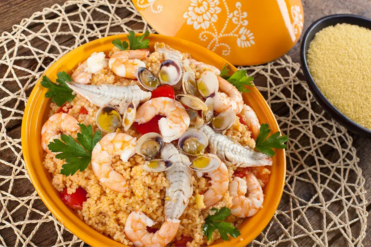 Un invitante cous cous di pesce, ricco di gamberi, vongole e pesciolini, guarnito con prezzemolo fresco.