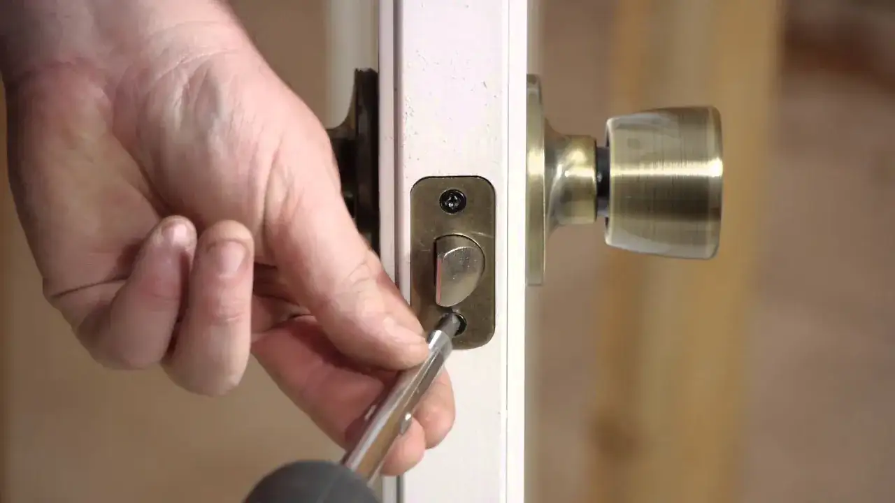 Mano desatornillando la placa de la cerradura de una puerta interior. Guía para como desmontar una cerradura de puerta interior.