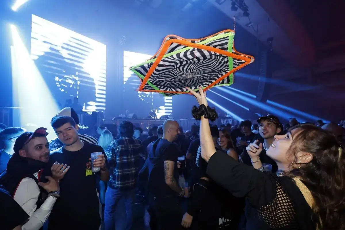 Gente disfrutando en el wake up festival, una mujer levanta un objeto con diseño psicodélico.
