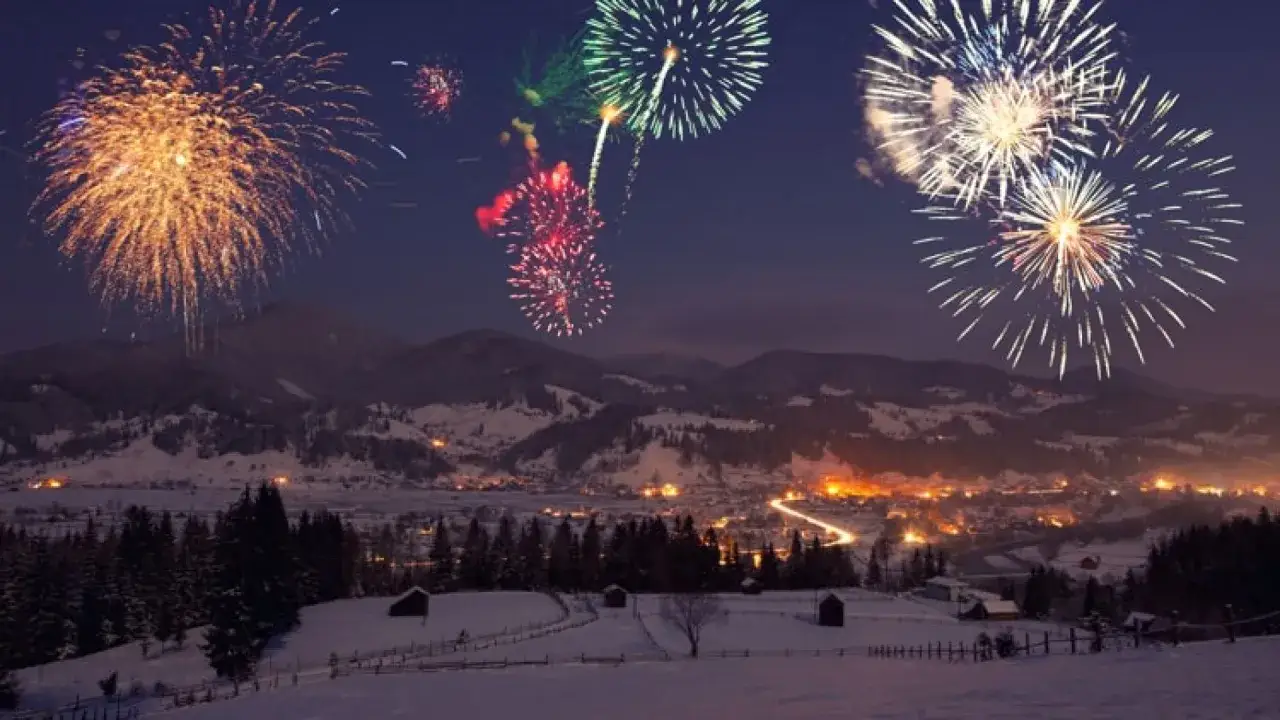 Fuochi d'artificio illuminano il cielo notturno sopra un villaggio innevato, celebrando il capodanno in montagna.