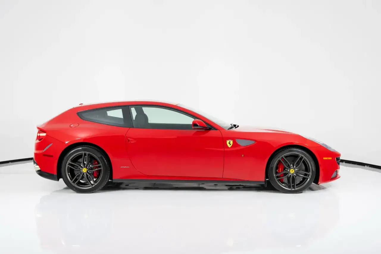 Czerwone Ferrari FF z czarnymi felgami i żółtym logo konia na błotniku, stojące na białej podłodze.
