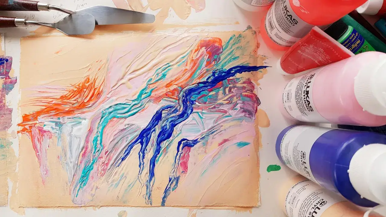 Peinture acrylique aux couleurs vives, avec des touches de bleu, orange et turquoise. Des spatules et des tubes de peinture sont disposés autour.