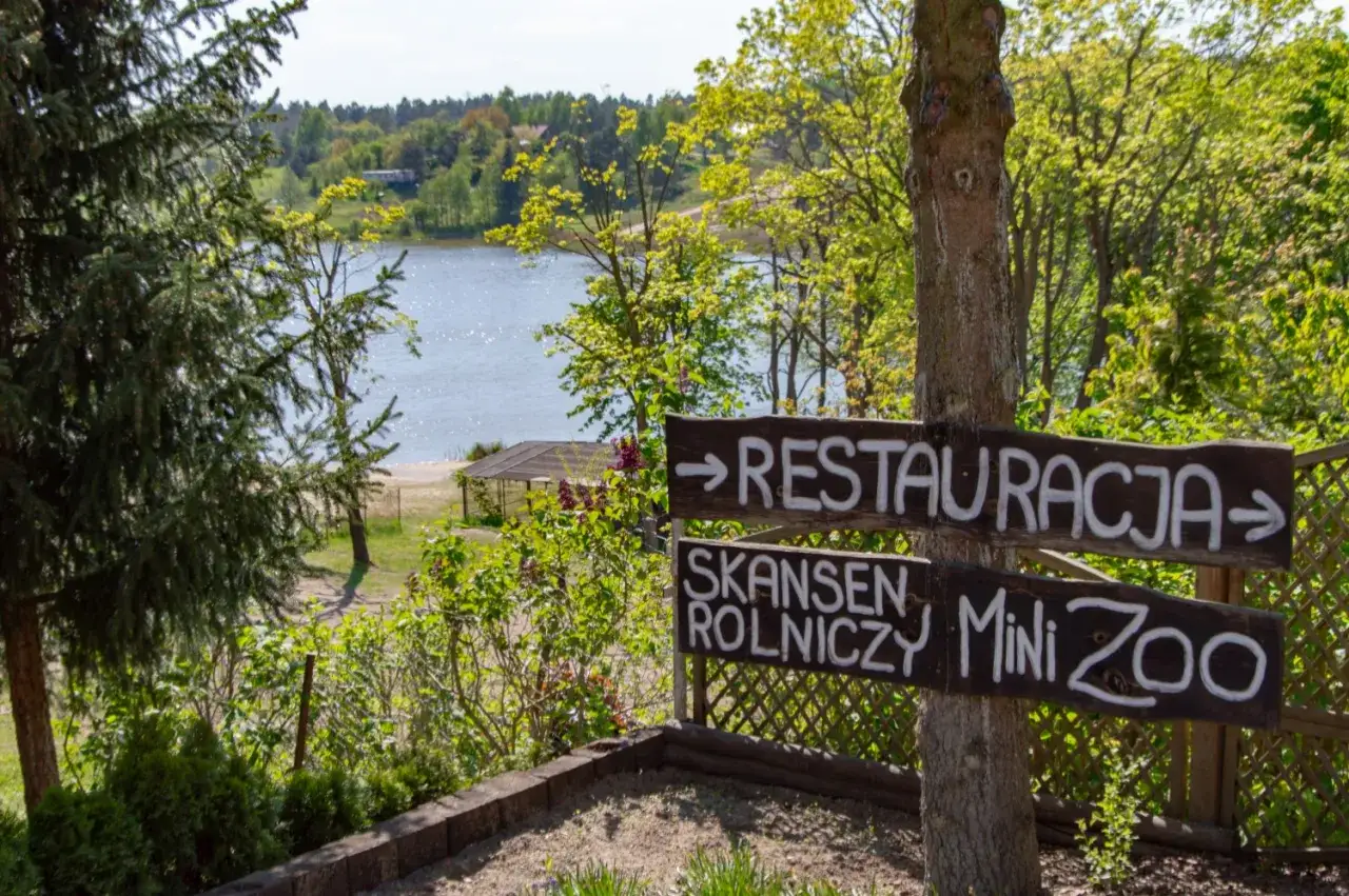 Drewniany drogowskaz wskazuje drogę do restauracji i skansenu z mini zoo. To świetne atrakcje na Kociewiu, nad jeziorem.