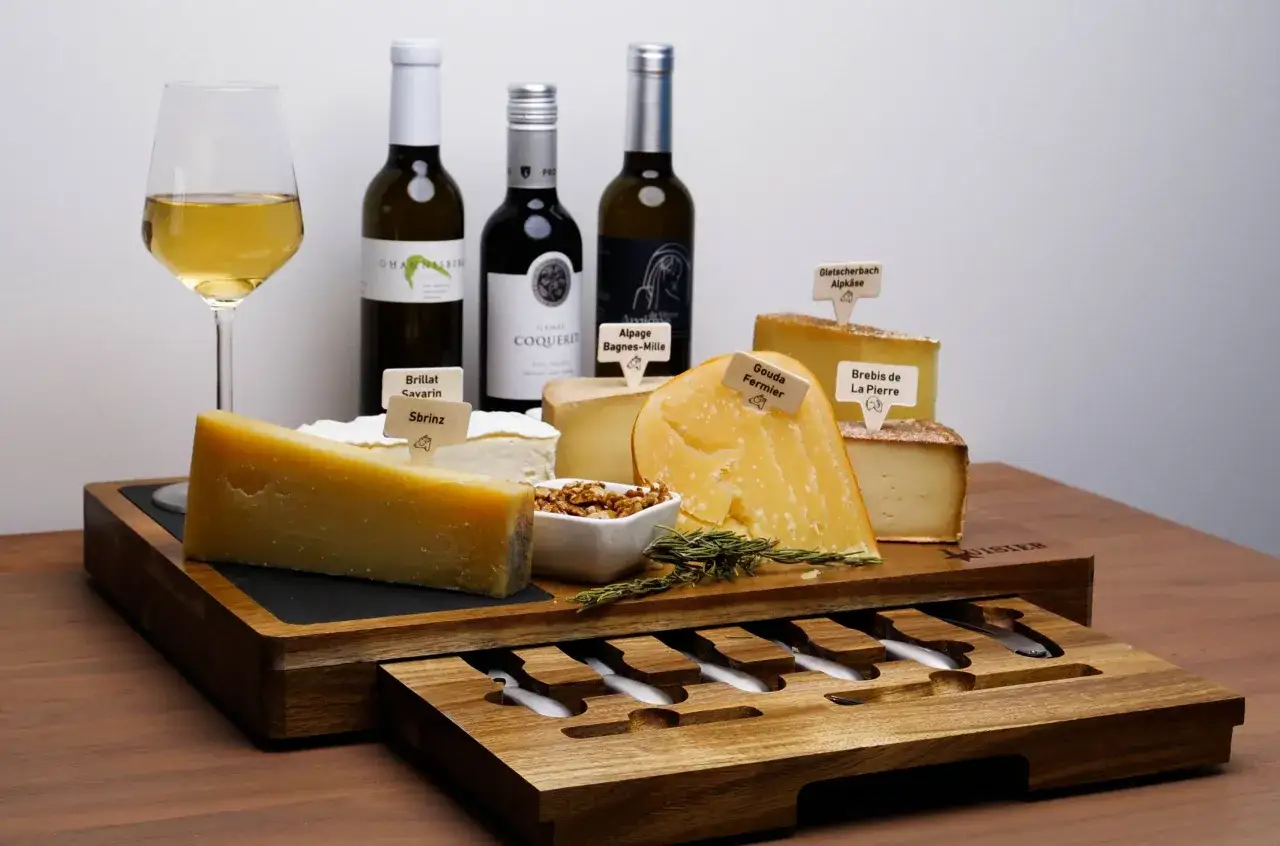 Un plateau de fromages variés avec des bouteilles de vin et un verre. Idéal pour savoir que boire avec du fromage.