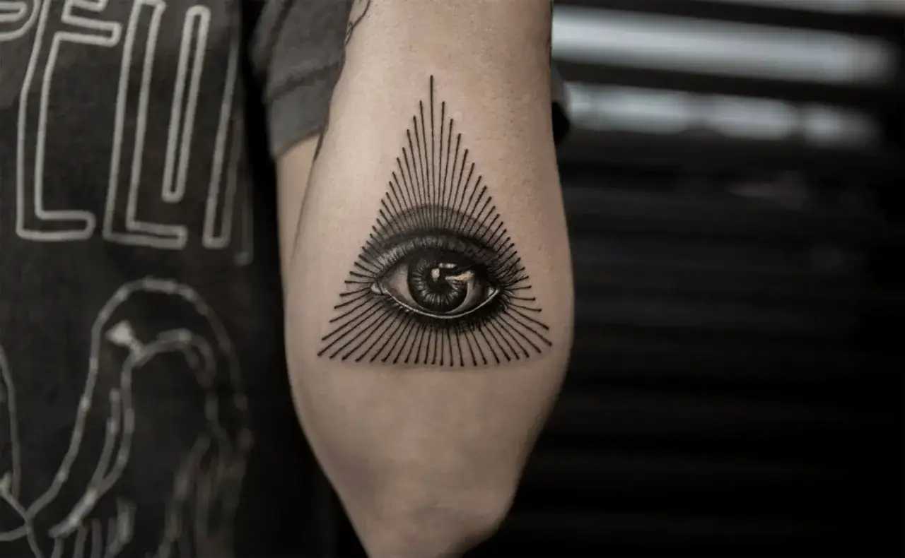 Oko proroka tatuaz na ramieniu, otoczone promieniami tworzącymi tr&oacute;jkąt.