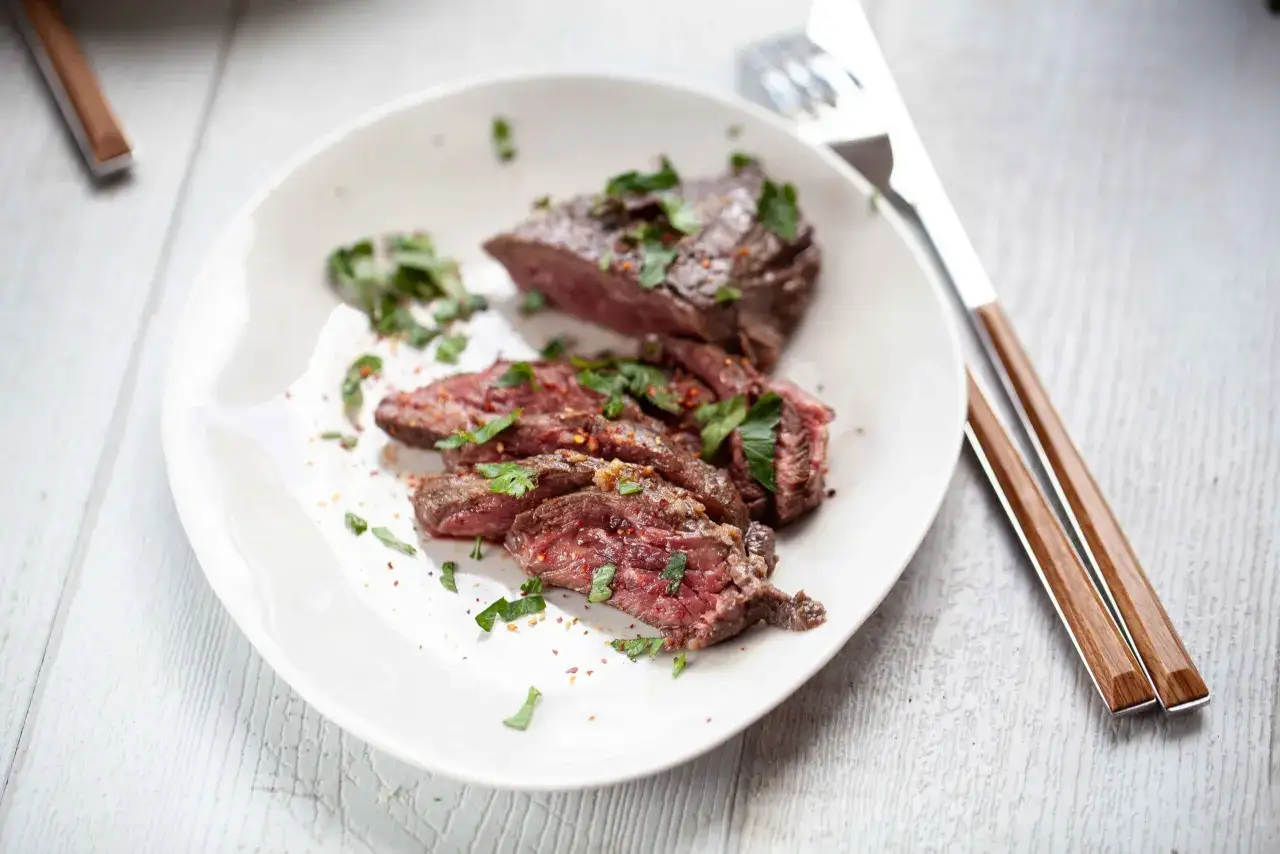 Délicieux onglet de boeuf recette, tranché et garni de persil frais et d'épices. Parfait pour un repas savoureux.