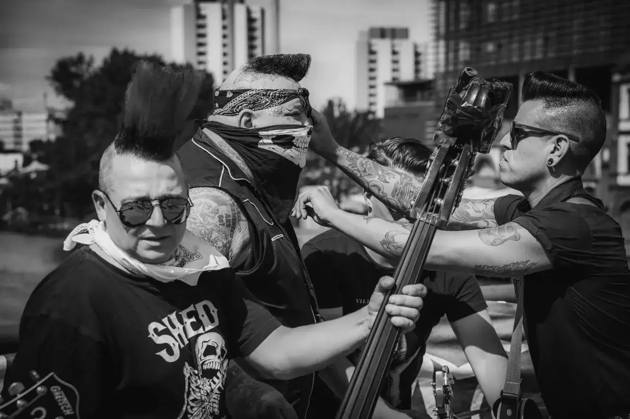 Quatre musiciens au look punk, dont un avec un bandana et un masque de cr&acirc;ne, se pr&eacute;parent &agrave; jouer. L'un d'eux tient une contrebasse, pr&ecirc;t &agrave; faire un 