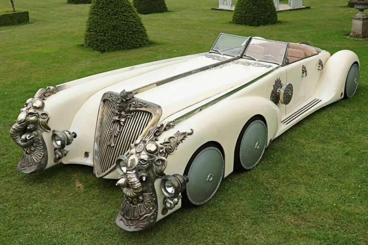 Ein cremefarbener Oldtimer mit Elefantenköpfen als Scheinwerferhalterungen, das seltenste Auto der Welt, steht auf einer gepflegten Rasenfläche.