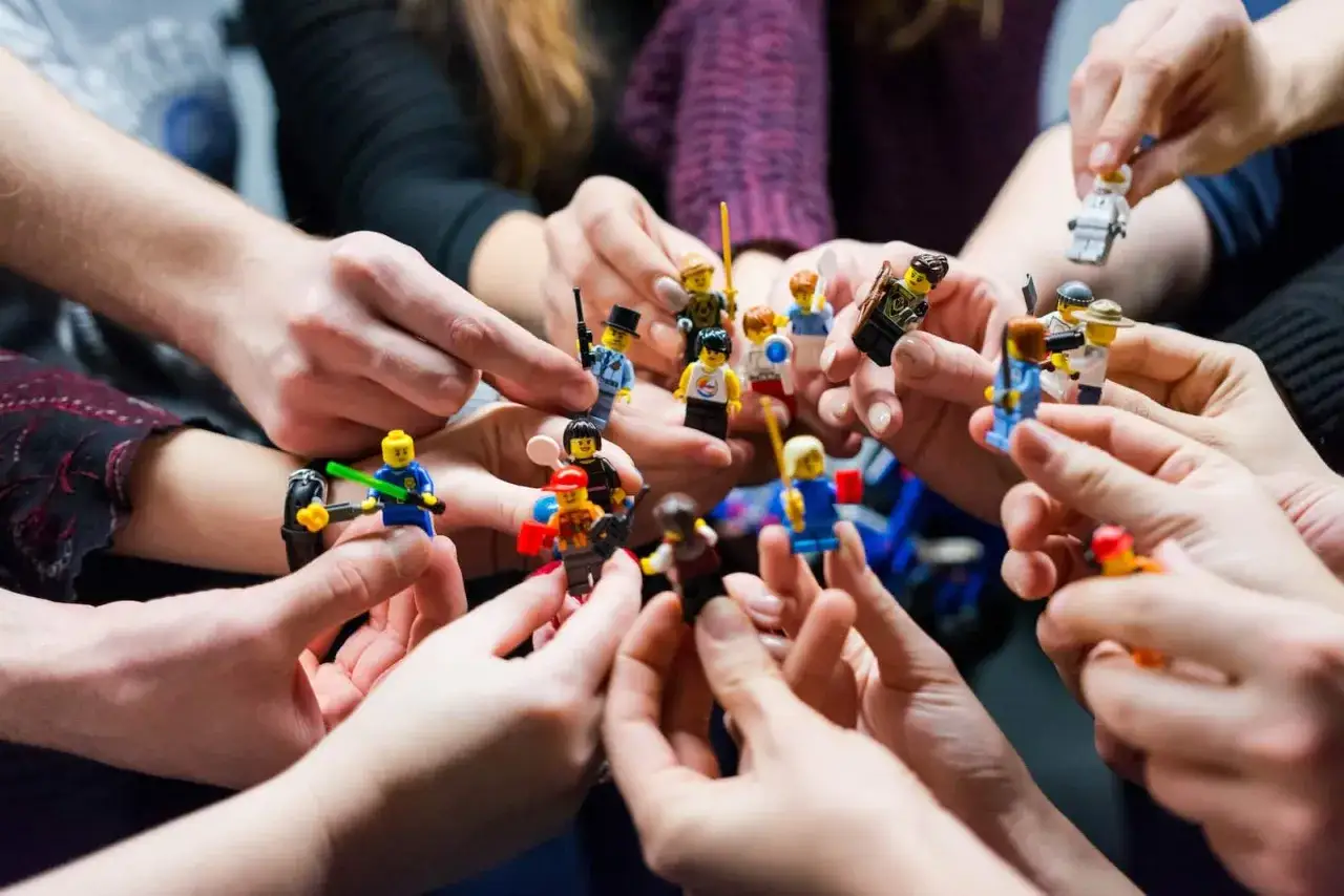 Des mains tiennent des figurines Lego, créant une scène de jeux d'intérieur en groupe.