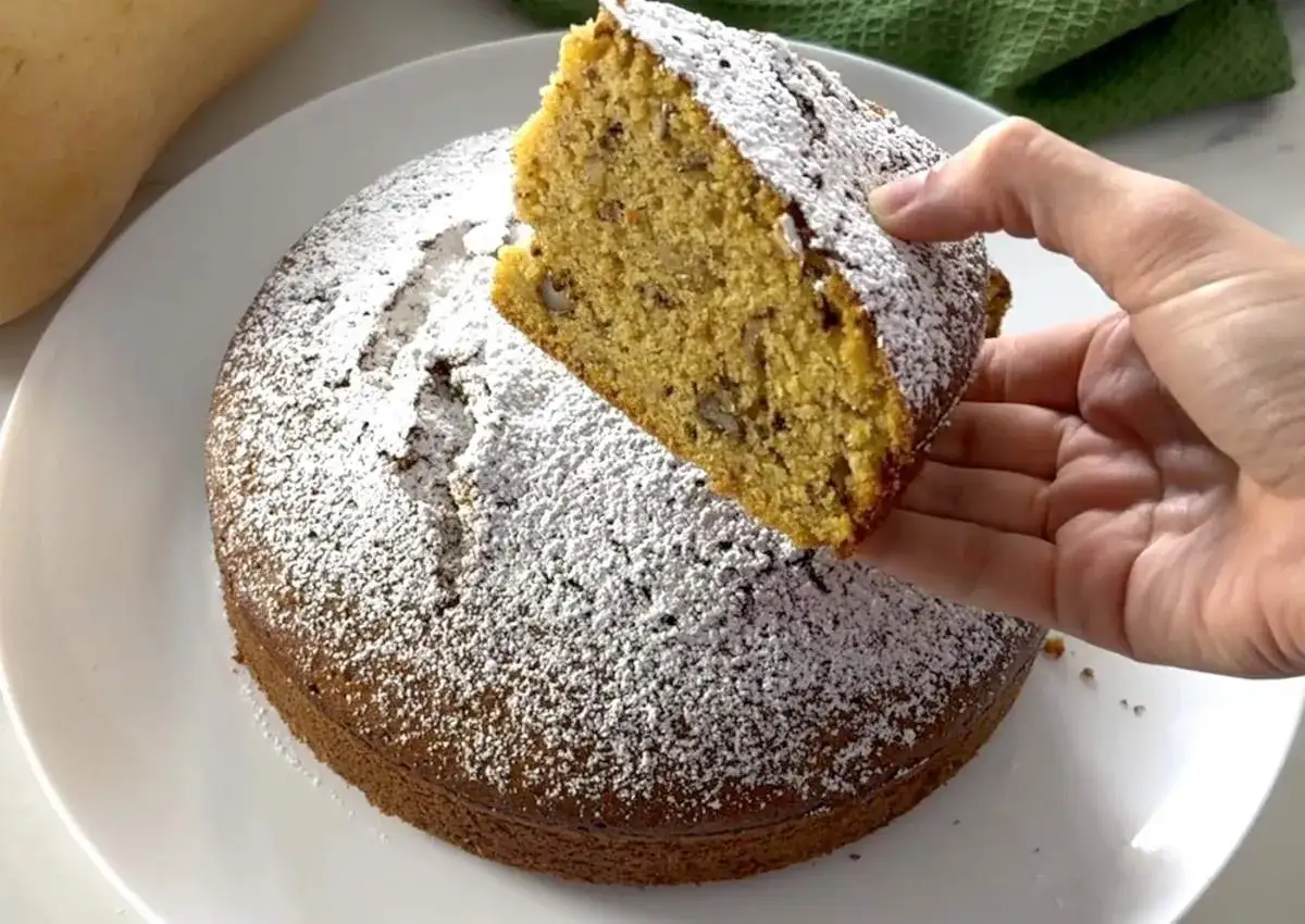 Un trozo de bizcocho de calabaza con nueces, espolvoreado con azúcar glas, se levanta de un bizcocho entero.