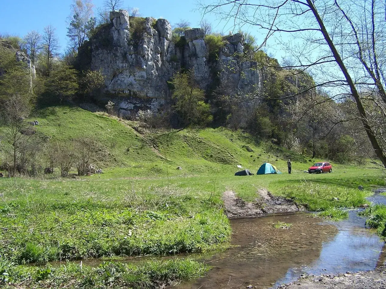 Malownicza dolina kluczwody z rozbitymi namiotami, czerwonym samochodem i strumieniem.